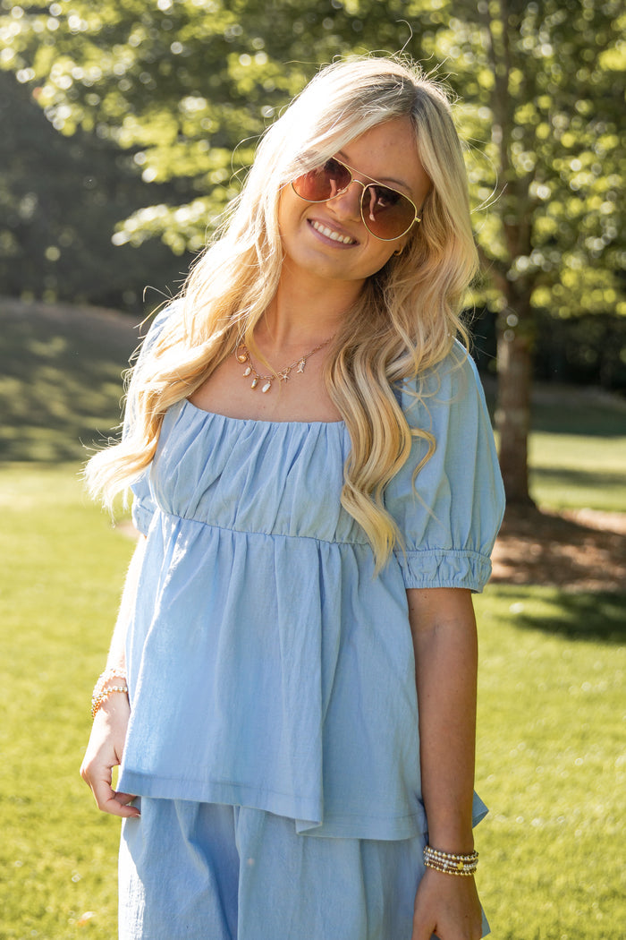 Woman wearing a light blue dress and sunglasses outdoors in a park