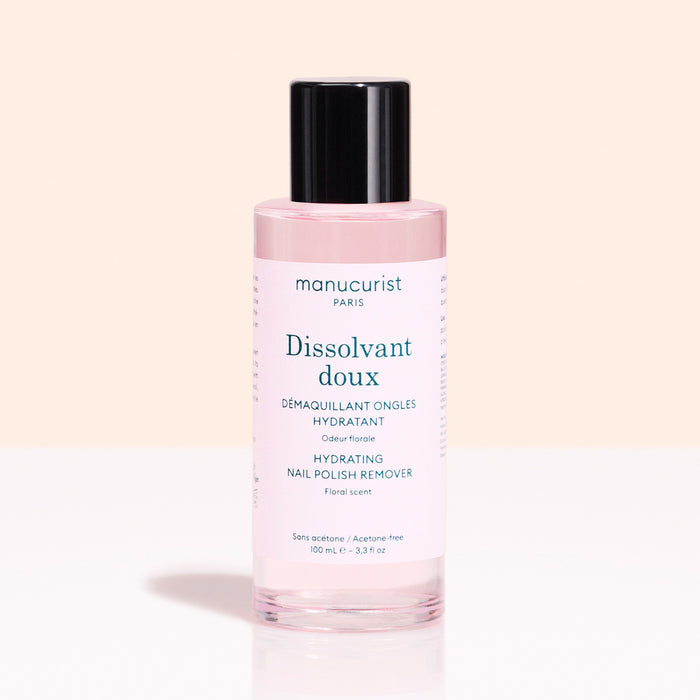 A pink bottle of Manucurist Gentle Remover with a black cap sits against a light pink background. The label notes it's acetone-free and floral scented.