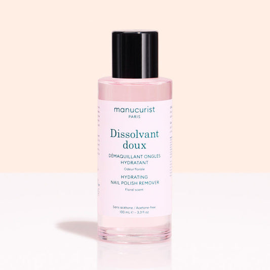 A pink bottle of Manucurist Gentle Remover with a black cap sits against a light pink background. The label notes it's acetone-free and floral scented.