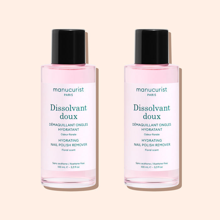 Two bottles of Manucurist Gentle Remover, featuring pale pink, acetone-free liquid with black caps and white labels, are placed side by side on a light beige background.