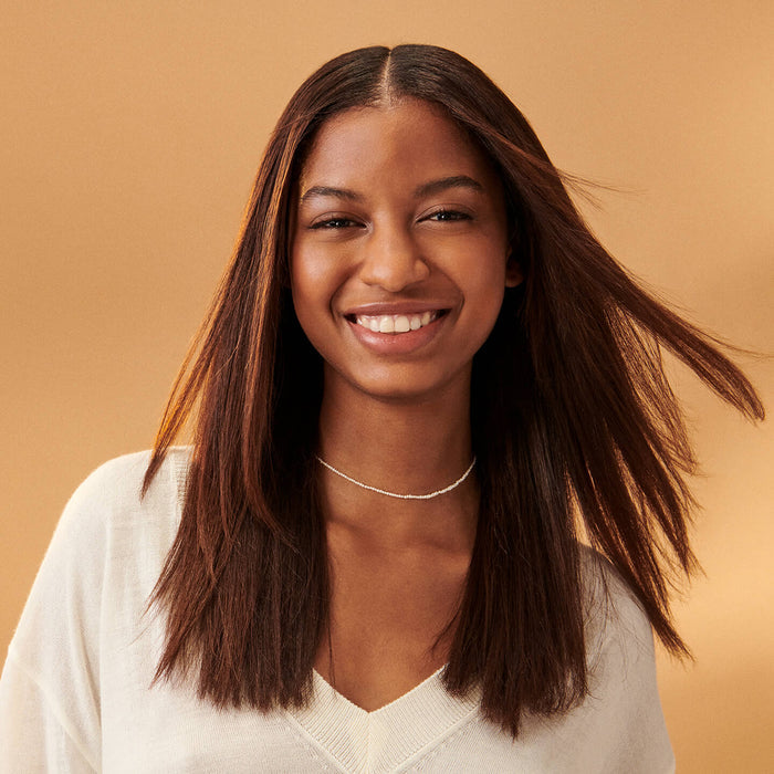 Dark skinned woman with long straight dark hair in white shirt on a yellow background.
