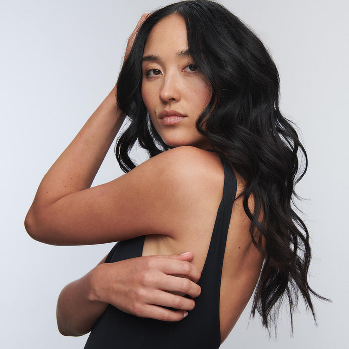 Woman with long black curly hair wearing a black tank top against a white background.