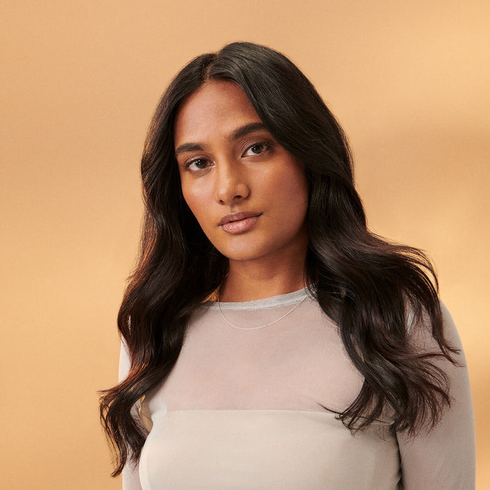 A dark skinned woman with long wavy dark hair on a beige background.