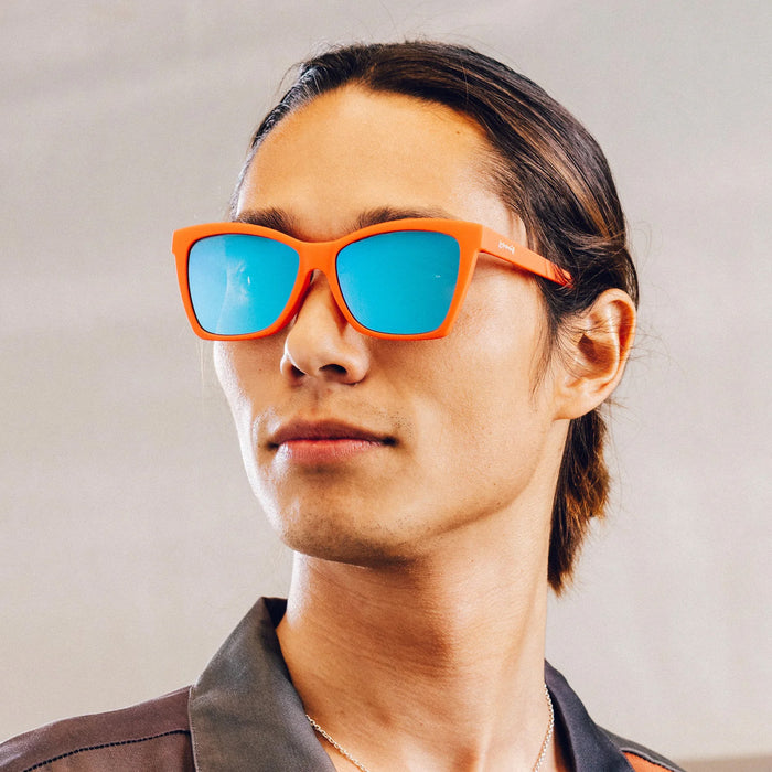 Person wearing orange sunglasses with blue lenses against a neutral background