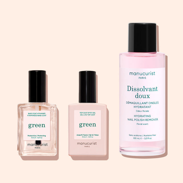 Three manicure products: two square bottles labeled Manucurist Green—one featuring the Vitaminized Base Coat Green™, a nail polish base coat with innovative KeraHCE+ technology to strengthen nails—and a tall, round bottle labeled Manucurist Dissolvant Doux containing pink liquid, all arranged on a light pastel background.
