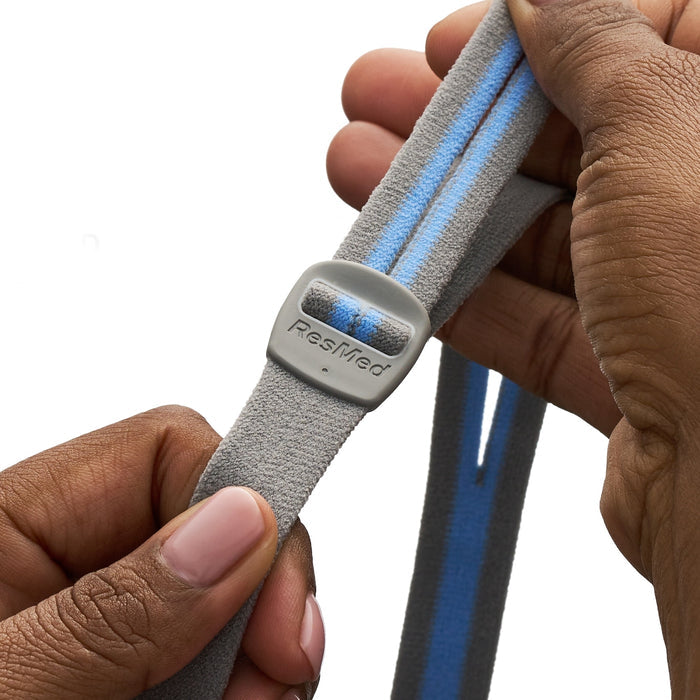 Gray strap with blue accents held by a hand, featuring the ResMed logo.