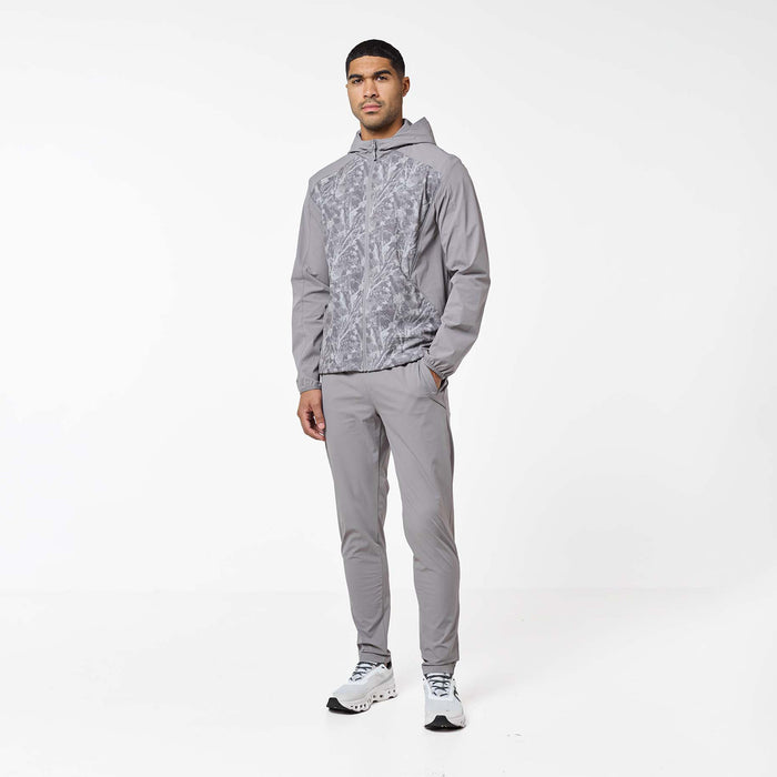 Model wearing the Ignite Tracksuit in Rock, featuring a printed panel hooded jacket with matching slim-fit pants and reflective detailing.
