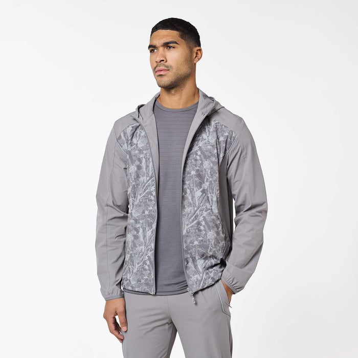 Model wearing the Ignite Tracksuit jacket in Rock unzipped, showcasing the printed front panels, three-piece hood and reflective piping details.