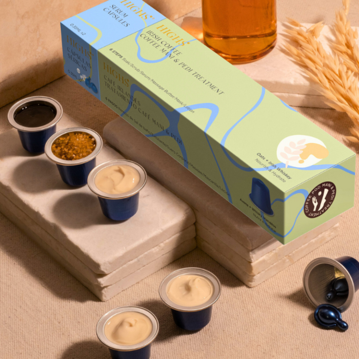 A packaged Irish Coffee Mani & Pedi Treatment with several small cups of a cream and scrub products, to be used for manicures and pedicures. The product box is labeled with 'Oats + Irish Whiskey' and has images of coffee beans and a whiskey bottle, indicating the treatment's theme and ingredients.