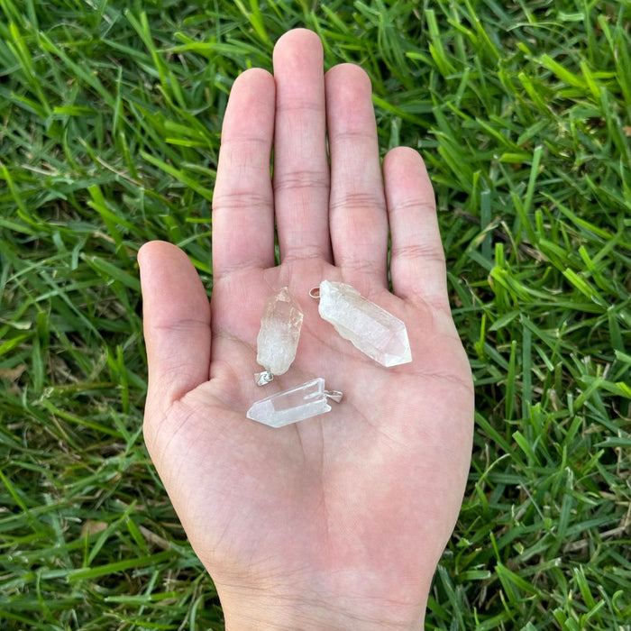 Three small clear crystal points resting on an open hand, photographed outdoors against a background of green grass.