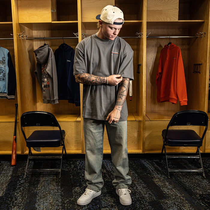 Person standing in a locker room wearing a gray t-shirt and pants.