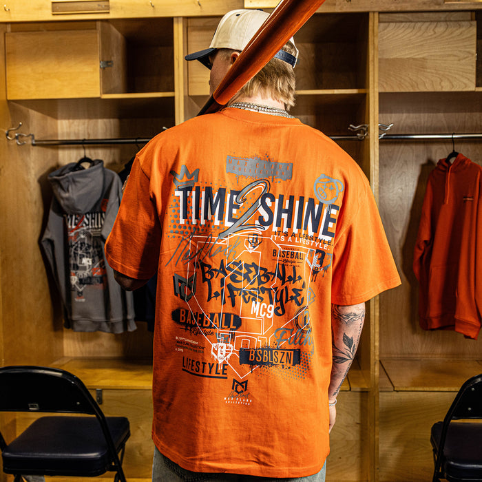Person wearing an orange 'Time 2 Shine' t-shirt in a locker room.