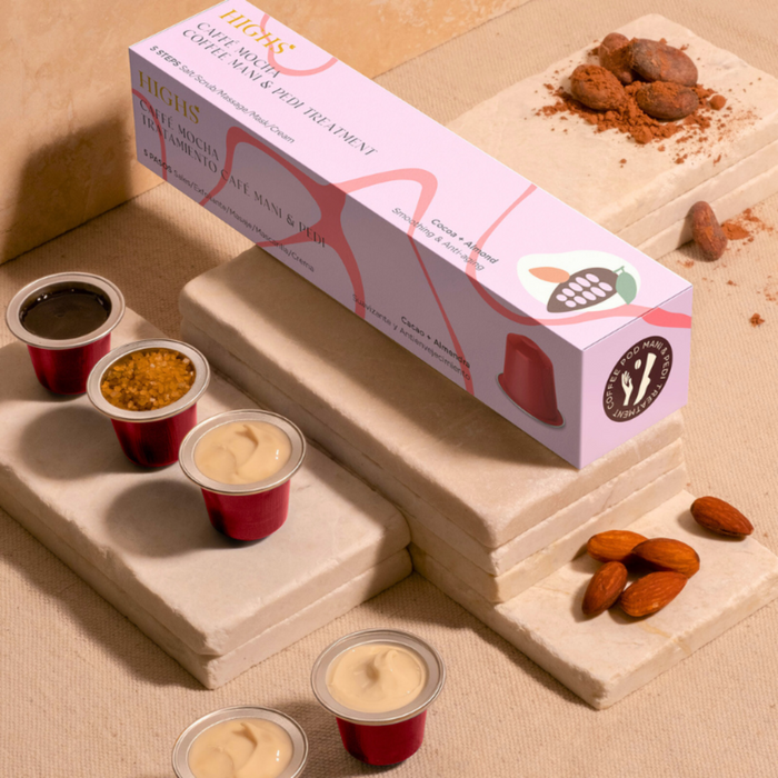 A set of products for a Mocha Mani & Pedi Treatment displayed on stones, including a box, pots with cream, coffee grounds, and almonds.