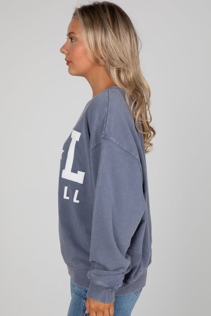 Woman wearing a blue sweatshirt with a large 'L' on the back against a gray background
