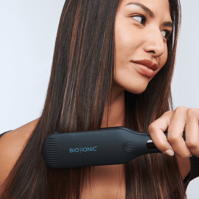 Woman with long dark hair using OnePass Styling Iron to straighten her hair