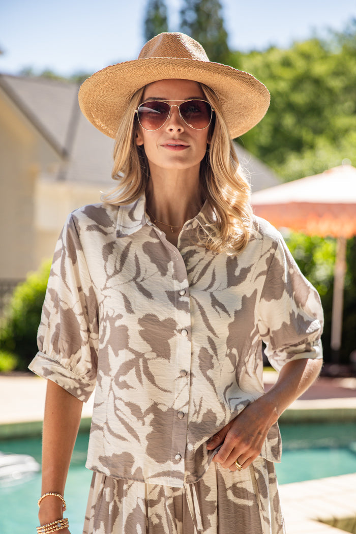 Woman wearing a patterned shirt and sun hat by a poolside