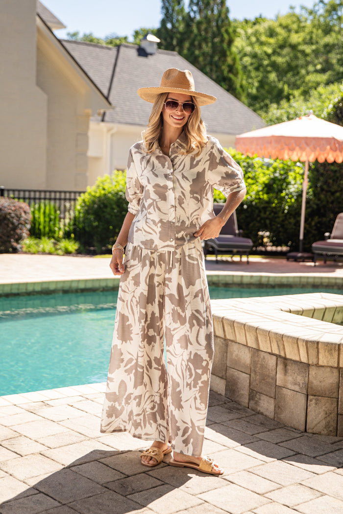 Woman in a floral fit and hat standing by a poolside.