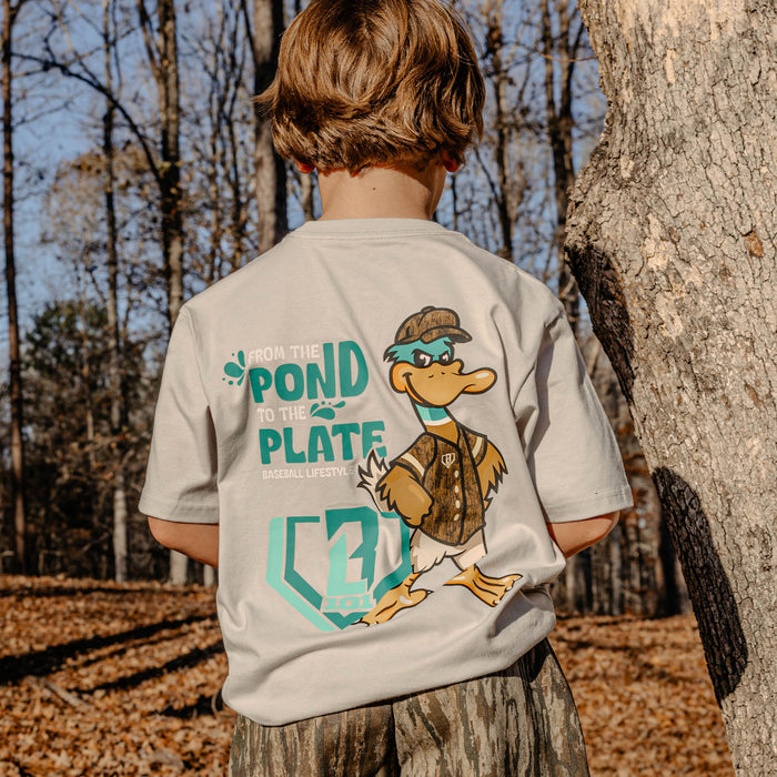 Child wearing a t-shirt with a duck graphic and 'From the pond to the plate' text in a forest setting