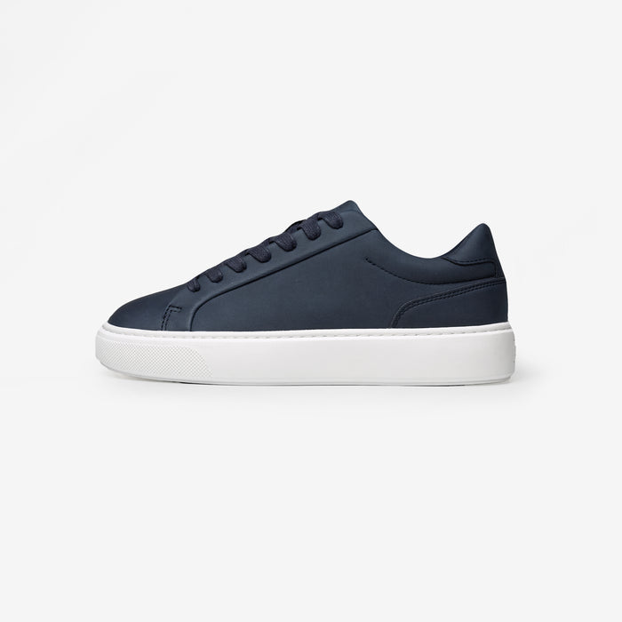 Side view of the Premium Classic Trainer in navy, featuring a clean white PU upper, navy faux suede heel, navy lace-up fastening and cushioned cup sole.