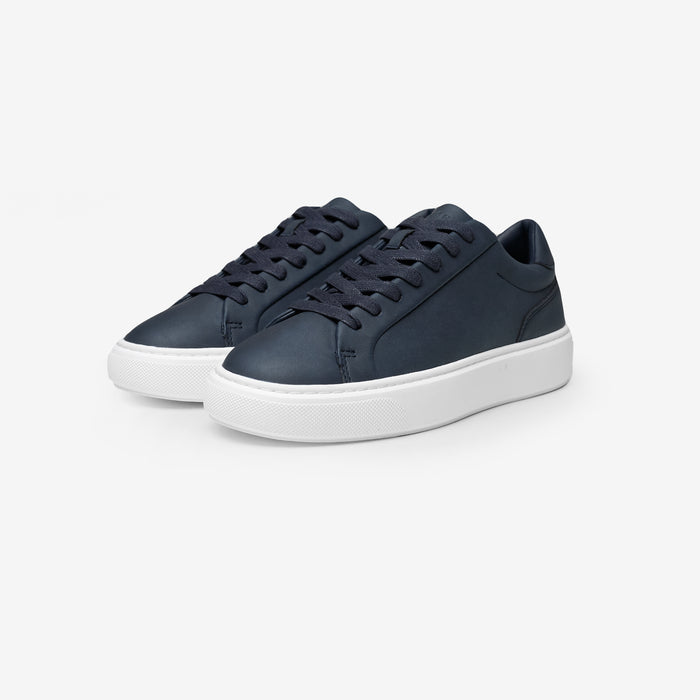 Three-quarter view of the Premium Classic Trainers in navy, featuring clean white PU uppers, navy lace-up fastening, navy faux suede heel panels and cushioned cup soles.