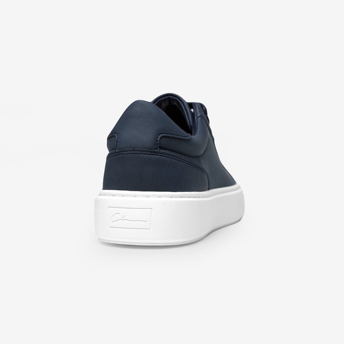 Rear view of the Premium Classic Trainer in navy, highlighting the navy faux suede heel panel and debossed Signature Closure London branding on the white cup sole.