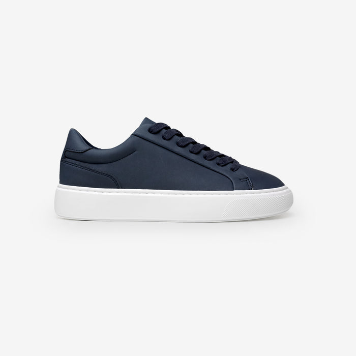 Side view of the Premium Classic Trainer in navy, featuring a clean white PU upper, navy faux suede heel, white lace-up fastening and cushioned cup sole.