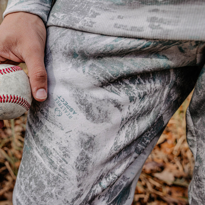Person holding a baseball with camouflage-patterned pants in an outdoor setting