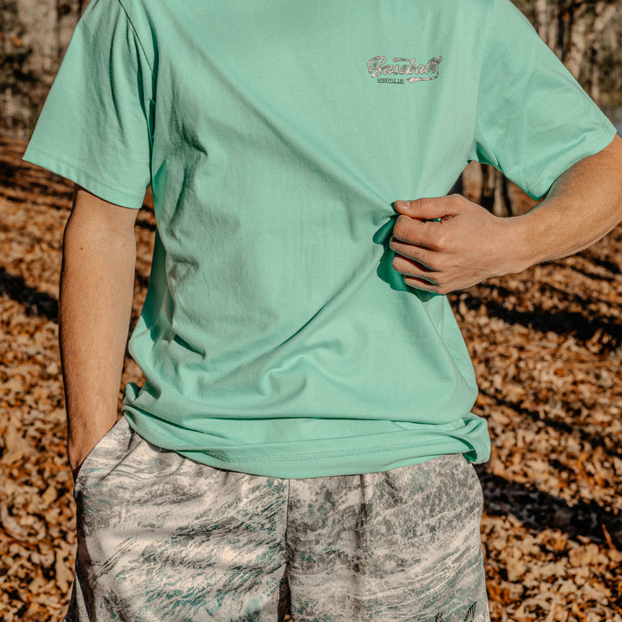 Man wearing a light green t-shirt with a Baseball Lifestyle 101 logo in a forest setting