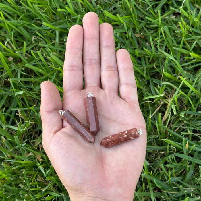 Red Jasper crystal point pendants displayed in the palm of a hand for size reference.