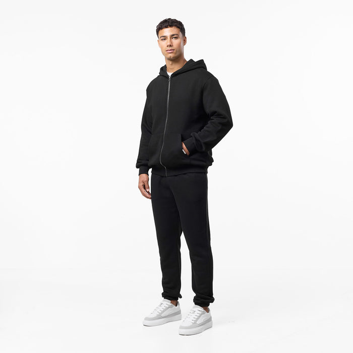 Front view of model in relaxed fit black tracksuit with zip up hoody and cuffed tracksuit bottoms