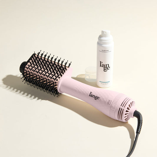 The Effortless Blowout Duo Value Set, featuring a Blush Le Volume Eleve brush and Glass Hair spray, displayed against a beige background
