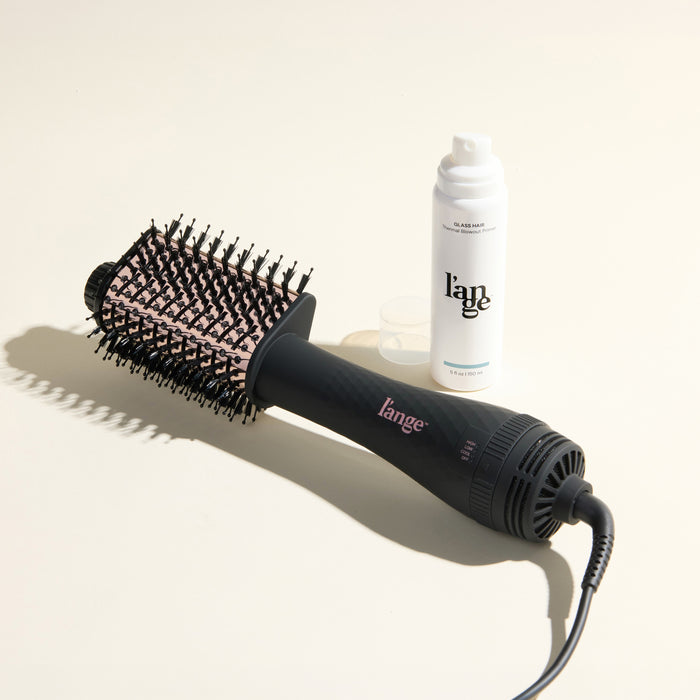 The Effortless Blowout Duo Value Set, featuring a Black Le Volume Eleve brush and Glass Hair spray, displayed against a beige background