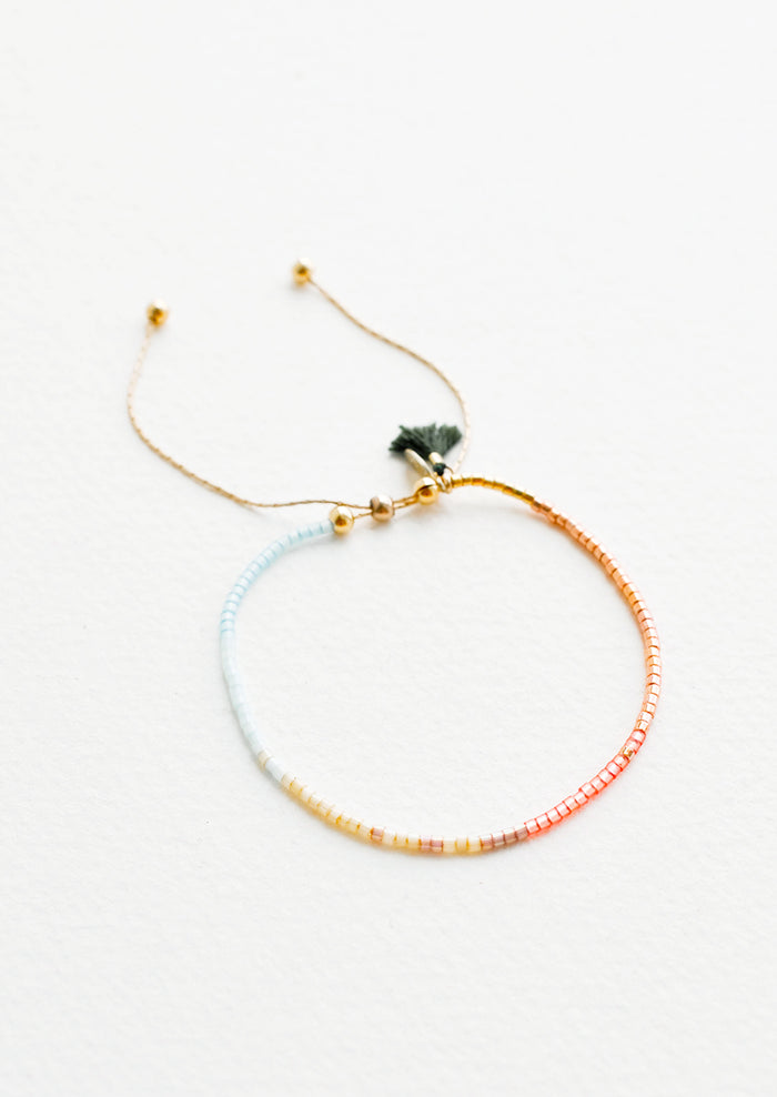 Delicate bracelet of glass beads in a gradient from pale blue to deep rust on a thin gold chain.