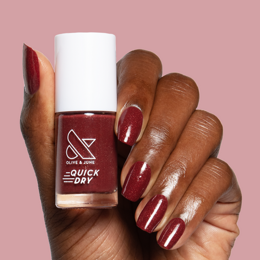 Saucy quick dry nail polish shown on hand with deep red shimmer mani against soft pink background
