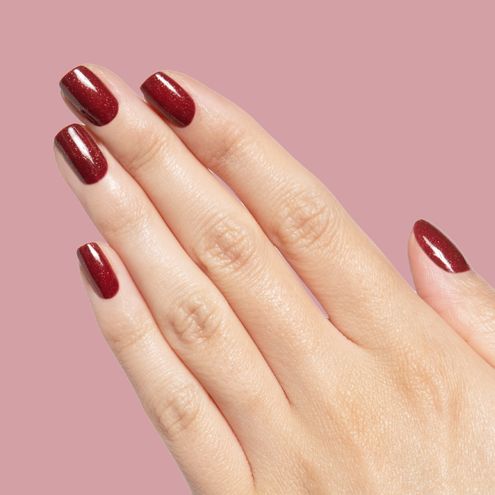 Saucy deep red quick dry polish with subtle shimmer on hand against soft mauve background showing manicure detail