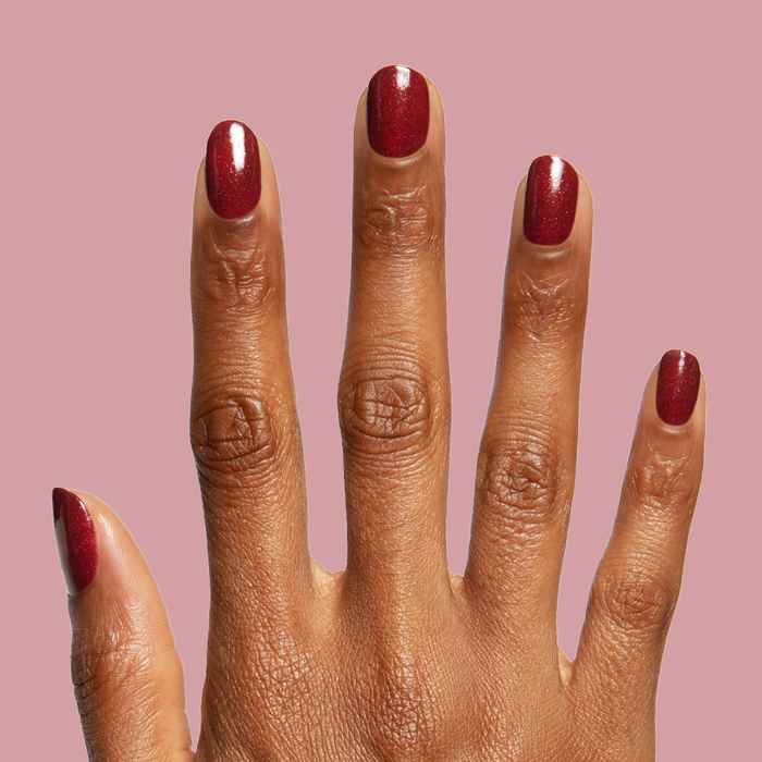 Saucy deep red quick dry polish with subtle shimmer shown on hand against muted rose background