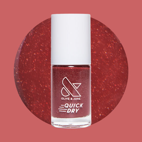Saucy deep red quick dry nail polish bottle with subtle shimmer shown on red glitter background