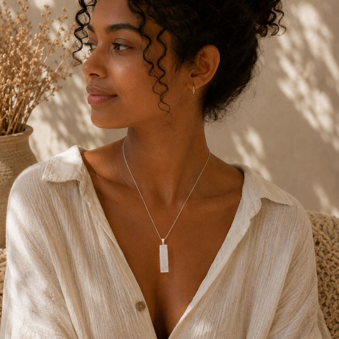 Person wearing a Raw Selenite point pendant on a delicate silver chain with neutral clothing in warm natural light.