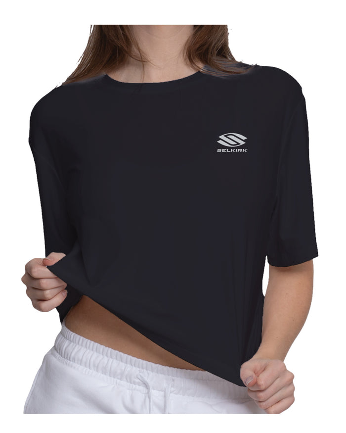 Person wearing black short-sleeve shirt with small white SELKIRK logo on left chest, holding the hem.