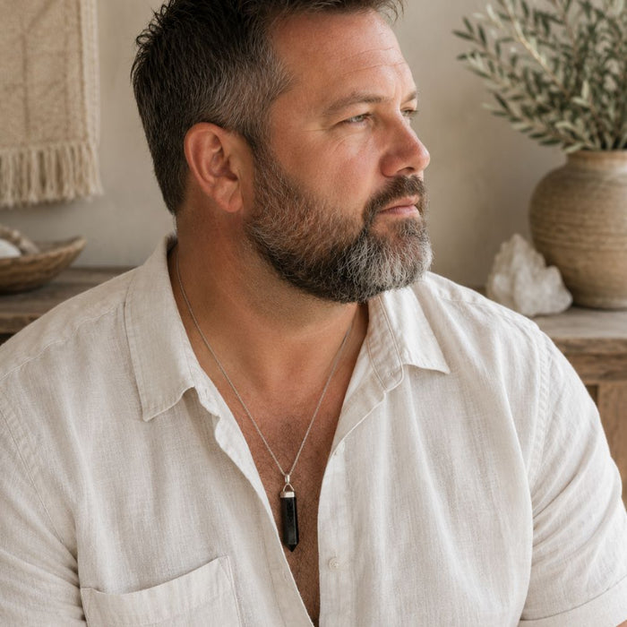 Man wearing a Shungite point pendant on a silver chain with a white linen shirt.
