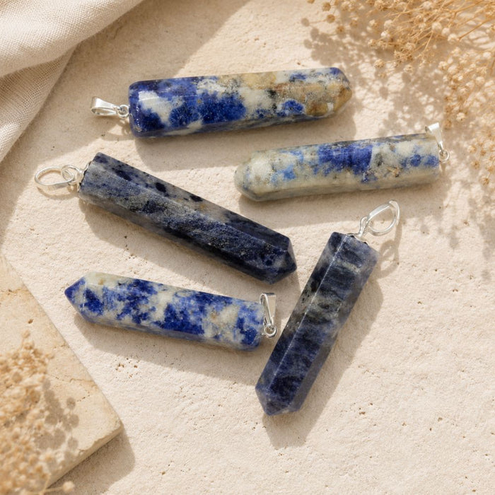 Sodalite crystal point pendants with silver loops on a neutral stone background.