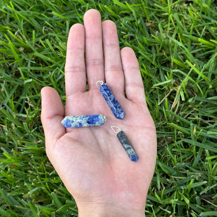 Sodalite crystal point pendants displayed in the palm of a hand for size reference.