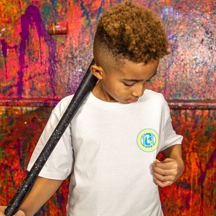 Child wearing a white t-shirt with BL101 logo, holding a baseball bat with a colorful background