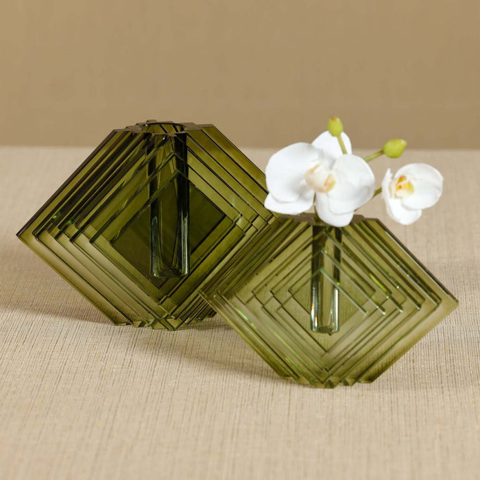 Two green geometric glass vases with a white orchid on a beige surface