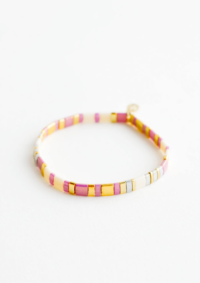 Bracelet featuring flat multicolor purple and cream glass beads interspersed with flat gold bead on an elastic cord.