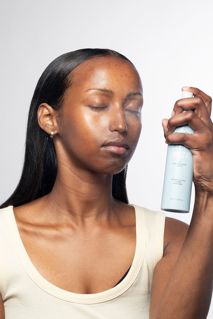 Woman applying a mist spray to her face against a plain background