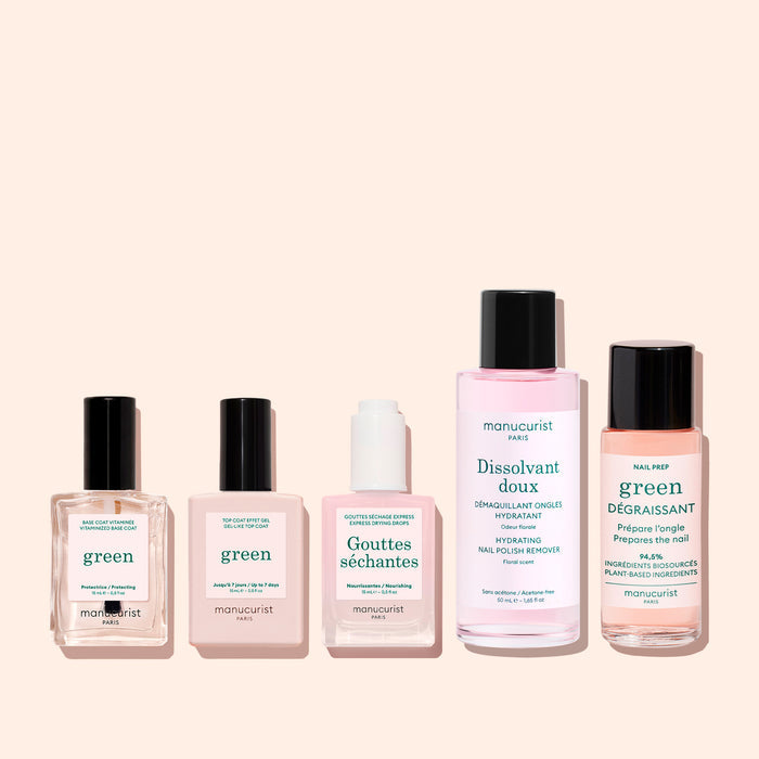 Five Manucurist bottles from The Essentials of the Green™ System, varying in size and shape with green, pink, and white labels, are arranged in a row against a light beige background. Featuring plant-based nail polish for a gel-effect manicure, this collection is a stylish and eco-friendly addition to your self-care routine.