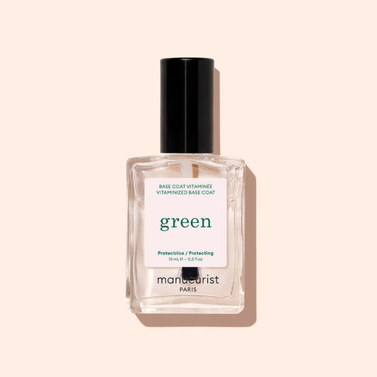 A clear glass bottle of Manucurist Vitaminized Base Coat Green™ with a black cap, photographed on a light beige background. Powered by KeraHCE+ technology, this base coat strengthens nails and creates the ideal foundation for your manicure.
